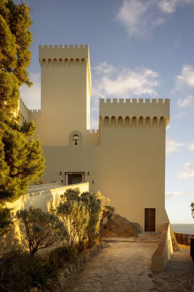 Le torri merlate di Castel Sonnino viste dal percorso in pietra d'accesso, tra pini e macchia mediterranea.