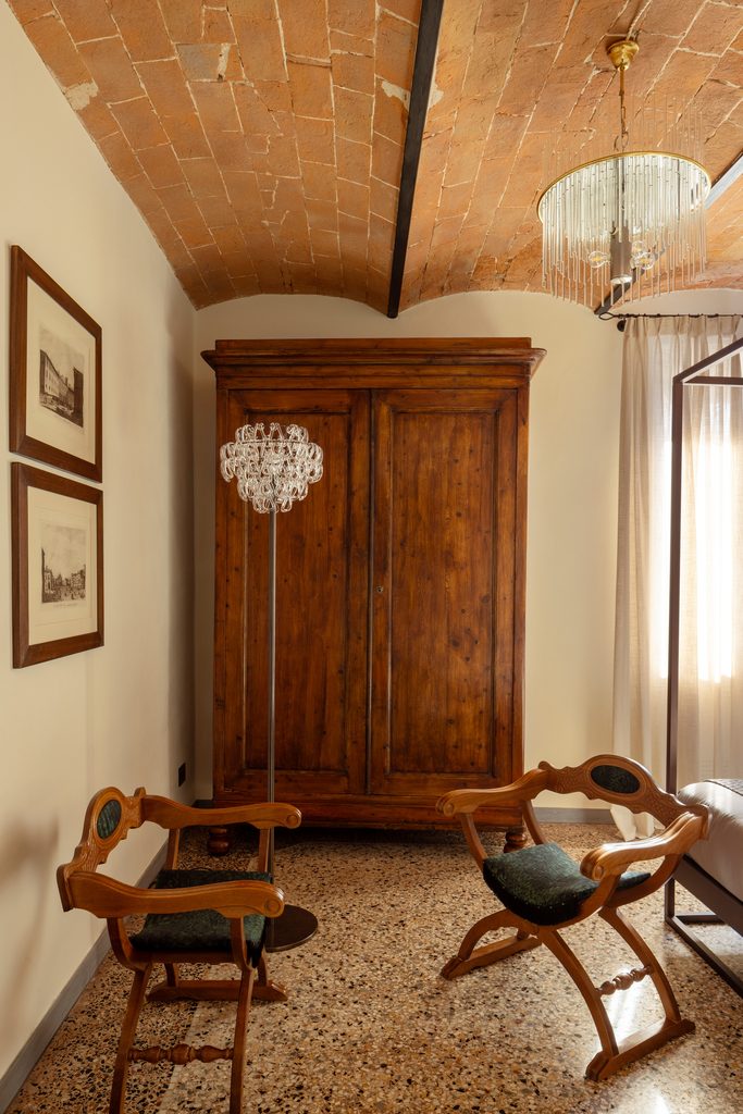 Stanza con armadio antico in legno, due sedie pieghevoli in legno e cuoio, lampada a sfere e pavimento in seminato veneziano.