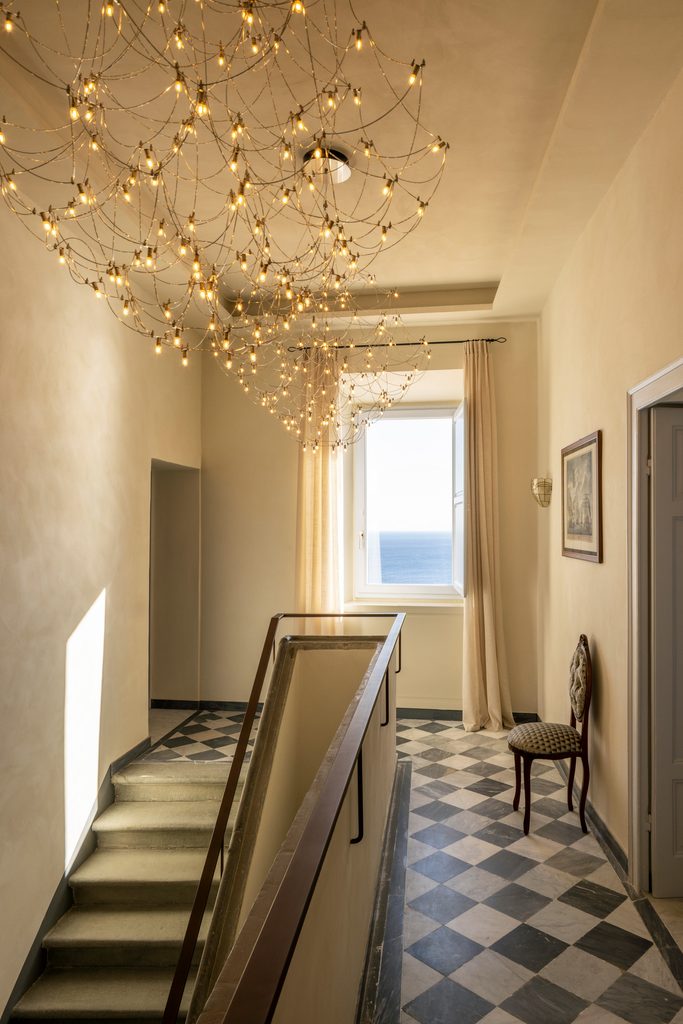 Pianerottolo della scala con lampadario a rete di piccole luci, pavimento a scacchi in marmo e finestra sul mare