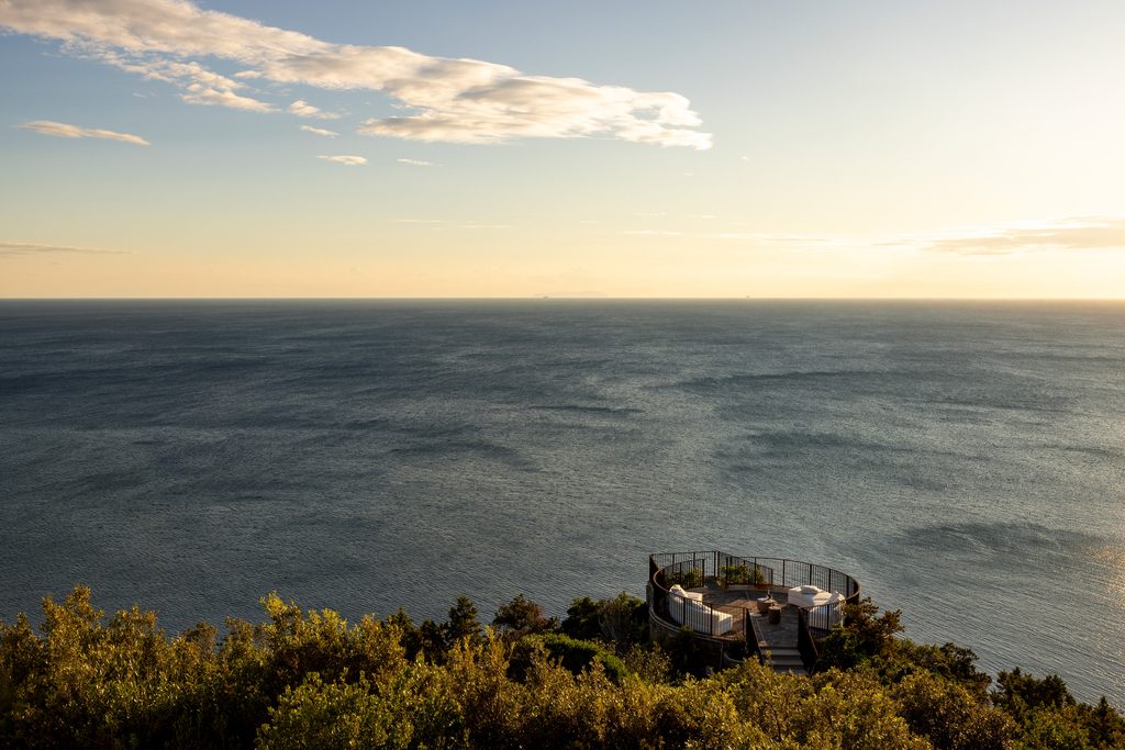 Terrazza circolare di Castel Sonnino sospesa sulla scogliera, con divani bianchi, davanti al mare al tramonto