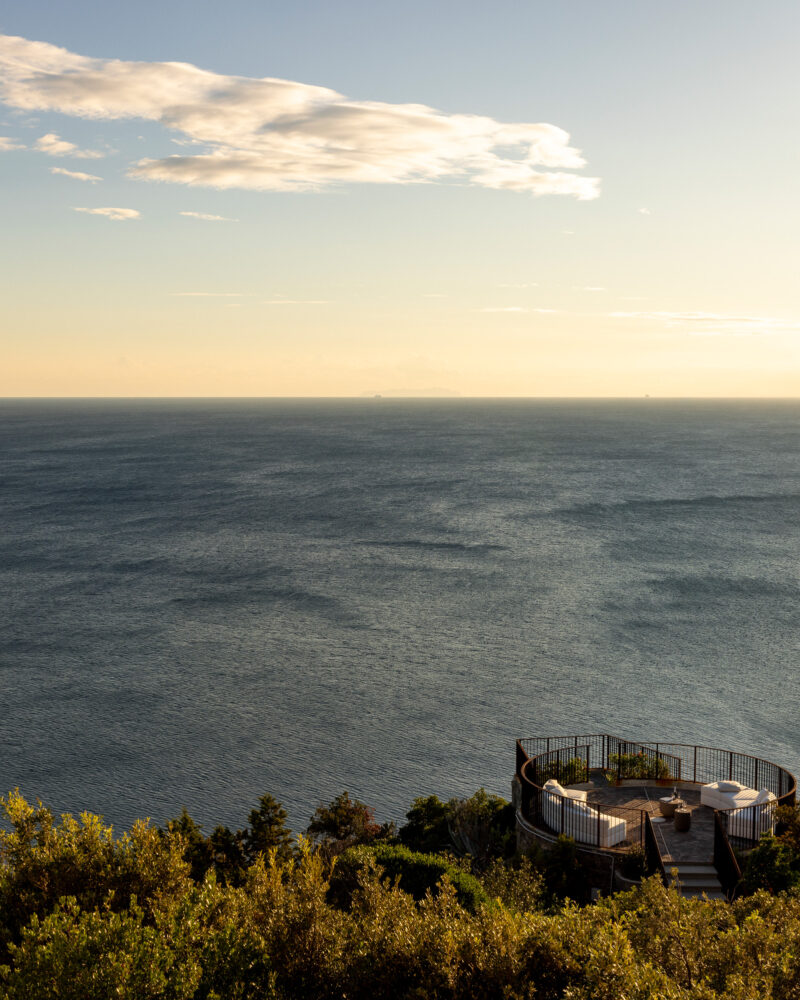 Terrazza circolare di Castel Sonnino sospesa sulla scogliera, con divani bianchi, davanti al mare al tramonto