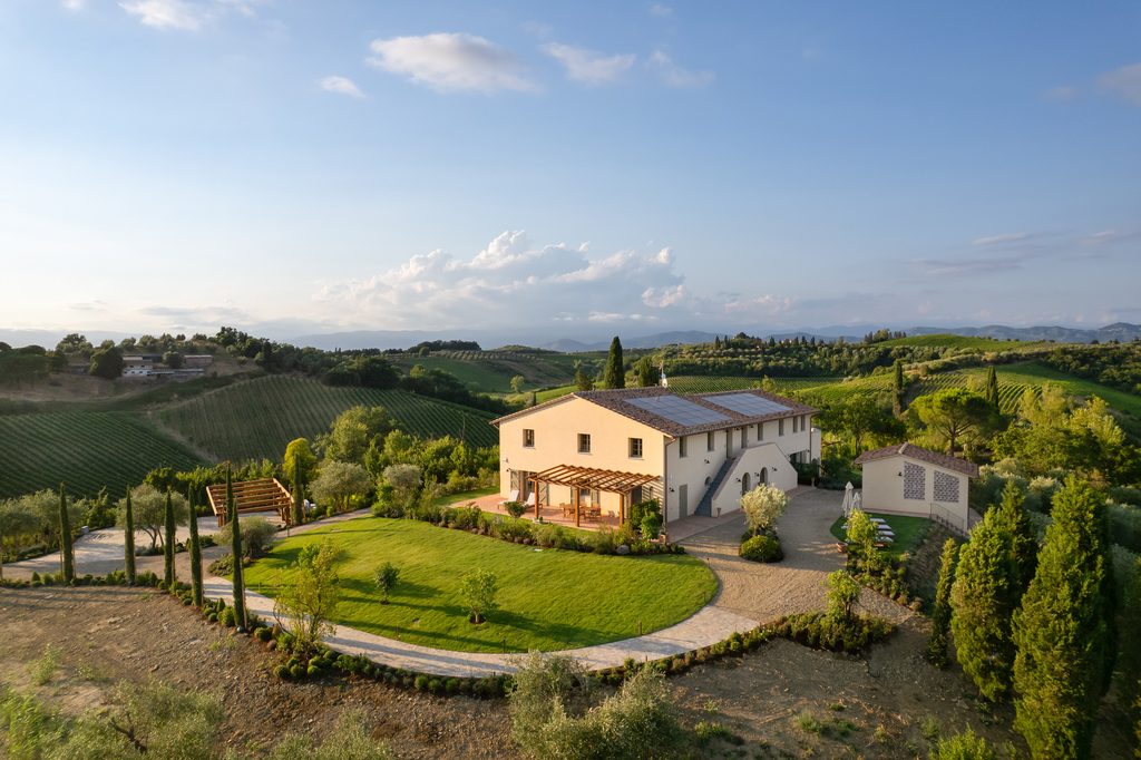 Vista aerea del casolare di Castelforno con il prato circolare, il percorso curvo bordato di cipressi e le vigne sulle colline intorno.