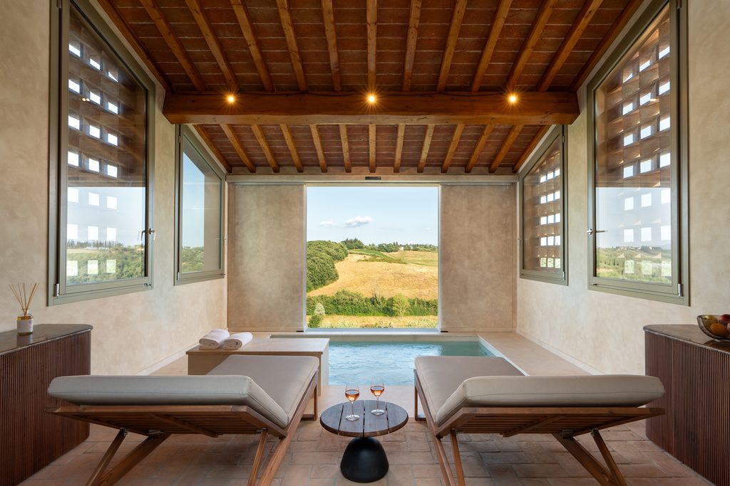 Piscina interna di Castelforno con due lettini, soffitto in travi di legno e cotto e grande apertura sulle colline di Cerreto Guidi.
