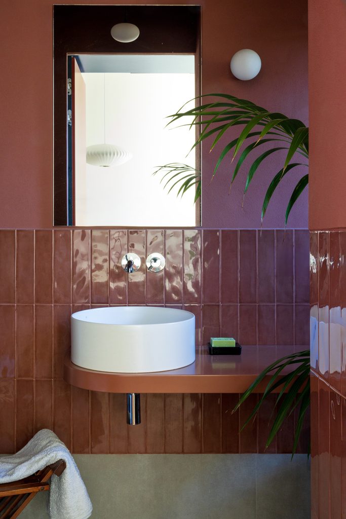 Bagno rivestito di piastrelle color terracotta, con lavabo rotondo da appoggio su una mensola curva e specchio a parete.