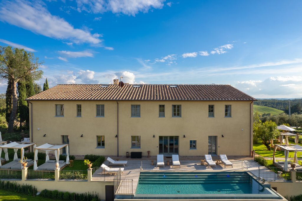Facciata del casale di Podere San Martino verso la piscina, con la pedana in legno, i lettini e le pergole ai lati.
