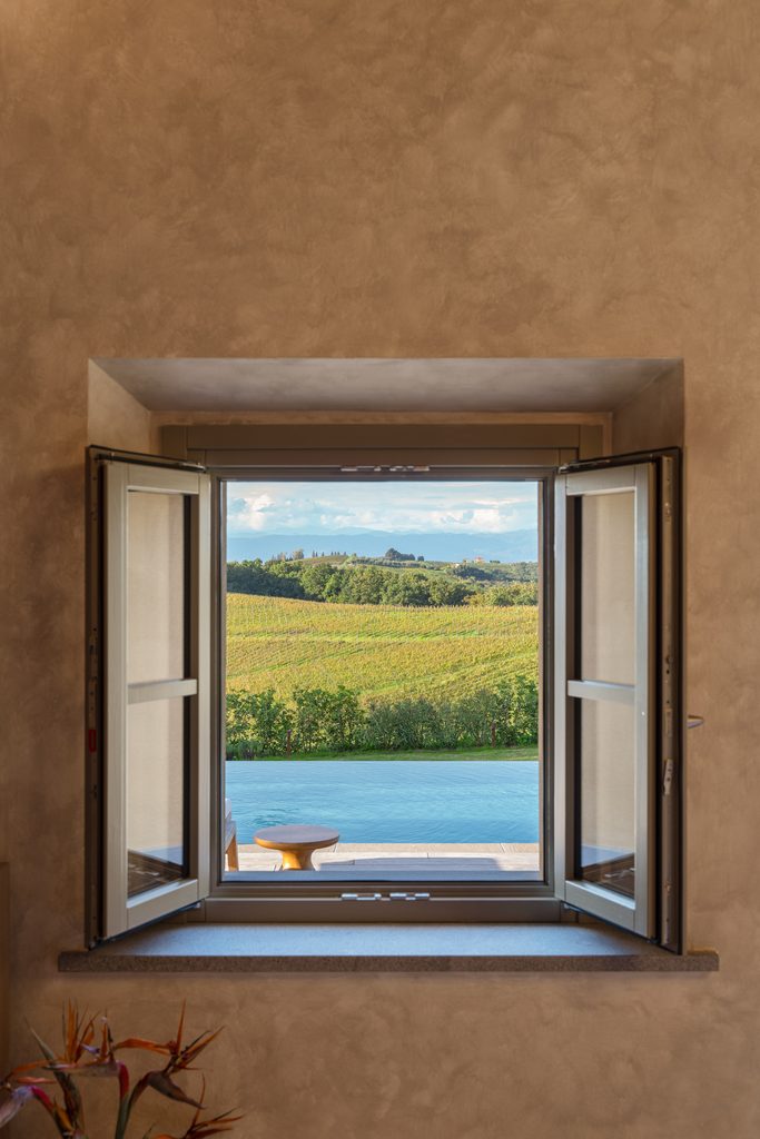 Finestra del casale aperta sulla piscina a sfioro e sulle vigne.